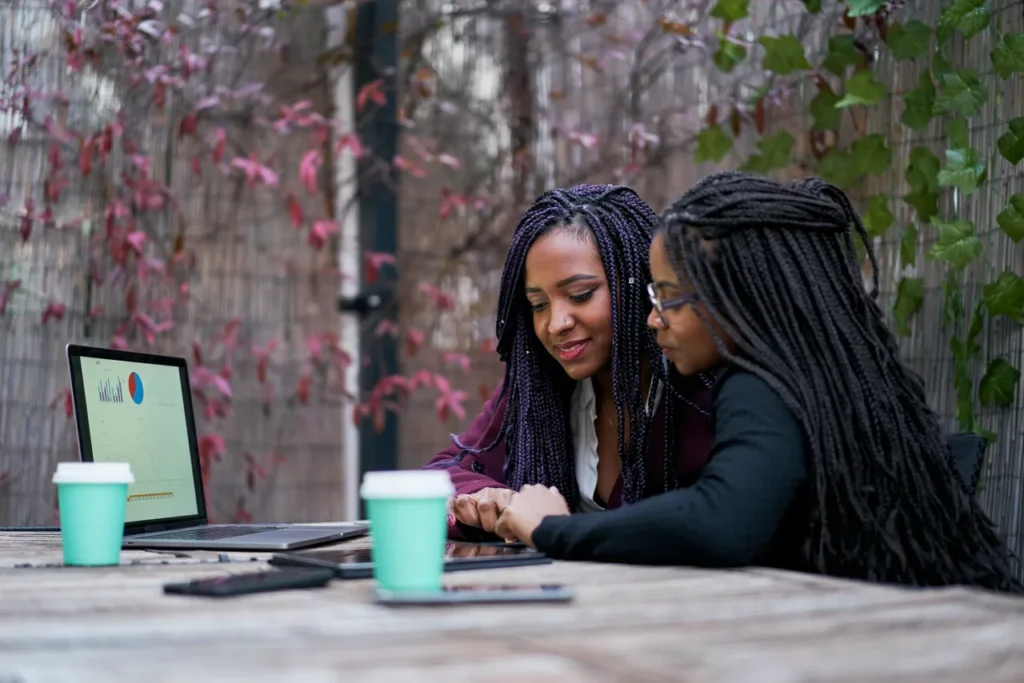 Two women sitting at a table with laptops.