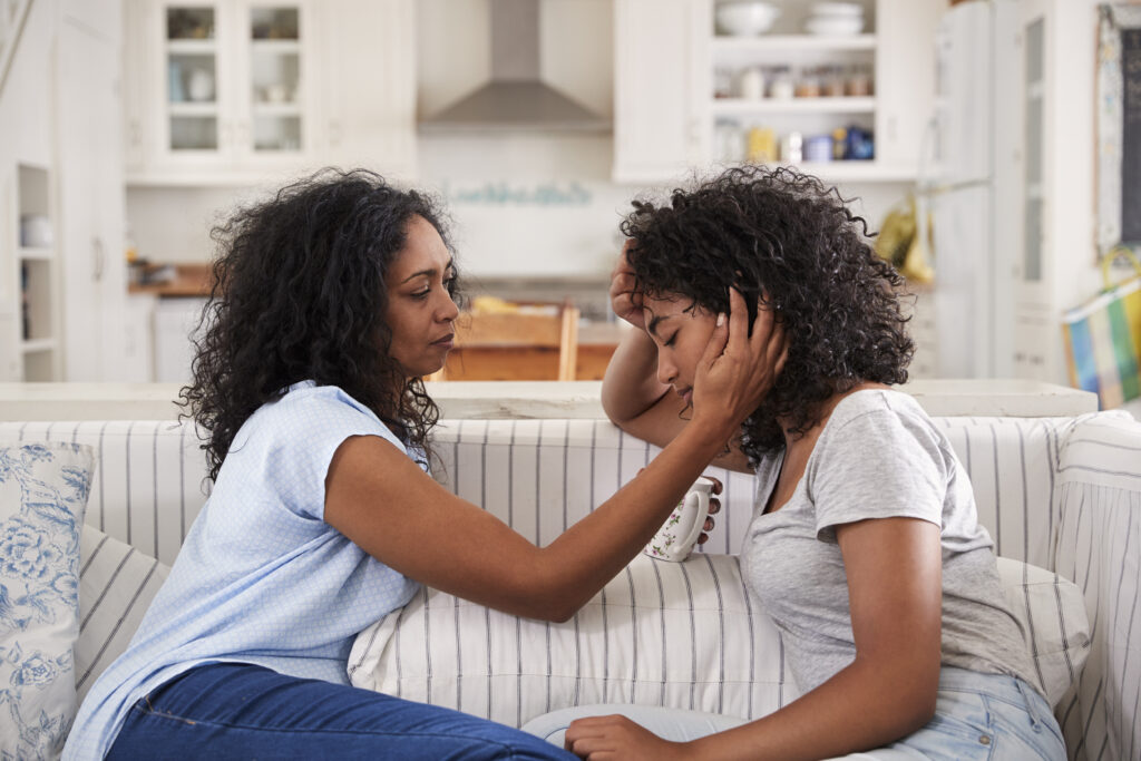 Two women sitting on a couch one is touching the other 's ear.