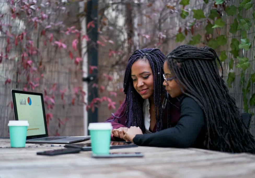 Two women sitting at a table with laptops.